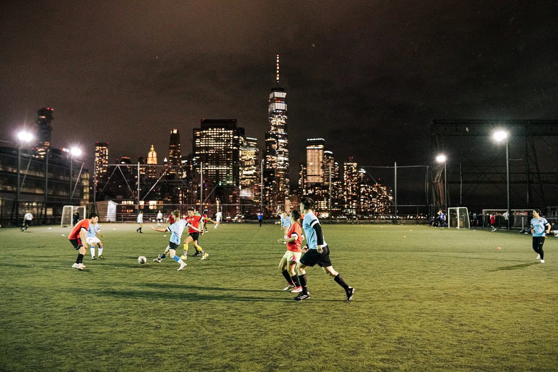 Night pickup game on a rooftop turf field with the lower Manhattan skyline behind
