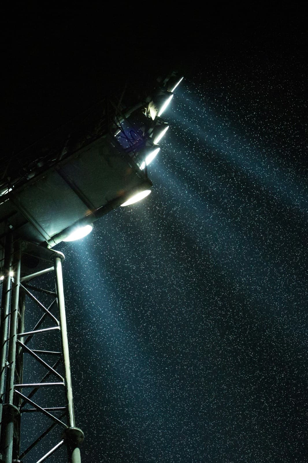 Field floodlights cutting through rain at a night game