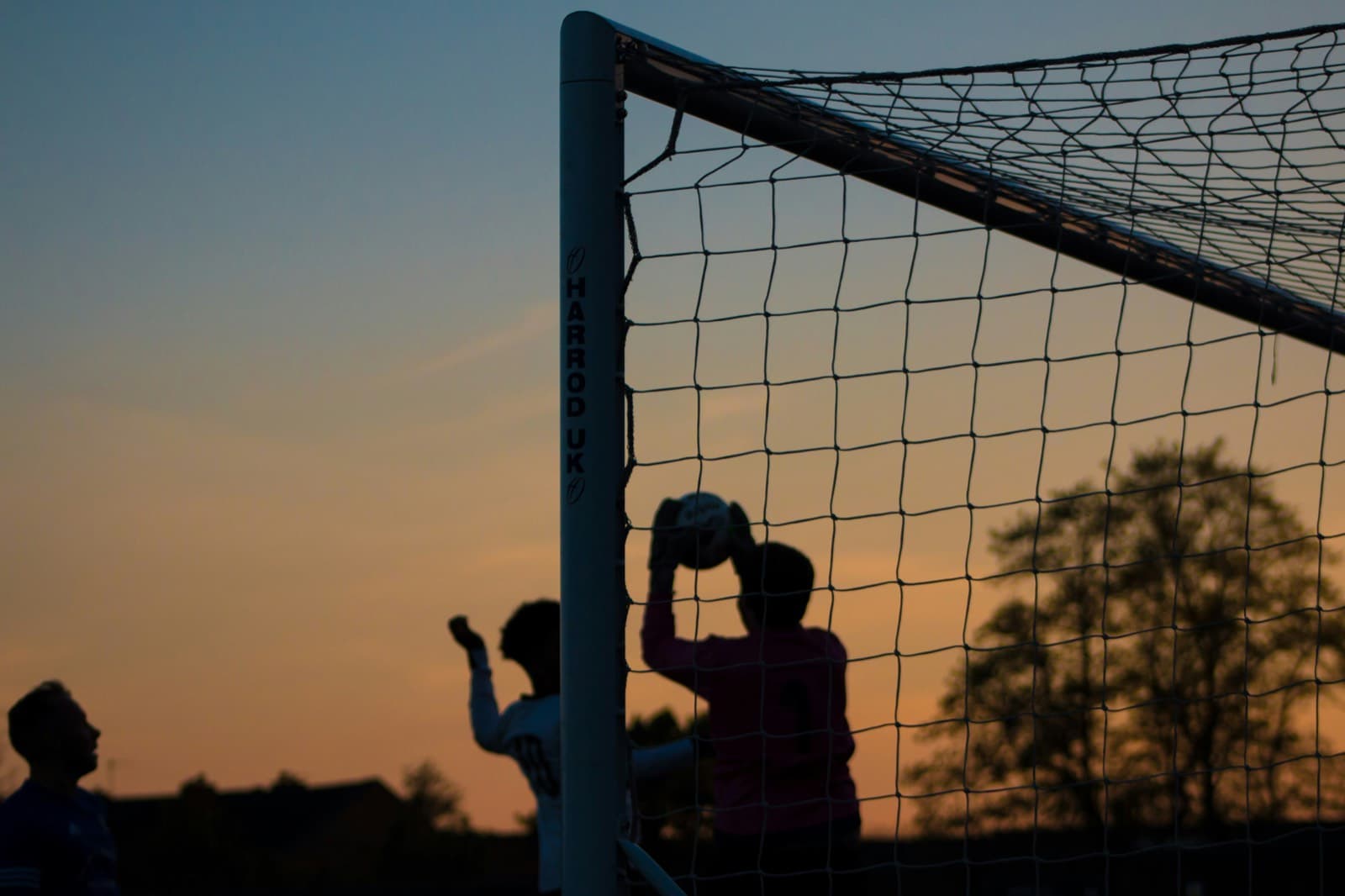 Keeper catching the ball at the near post against a sunset sky